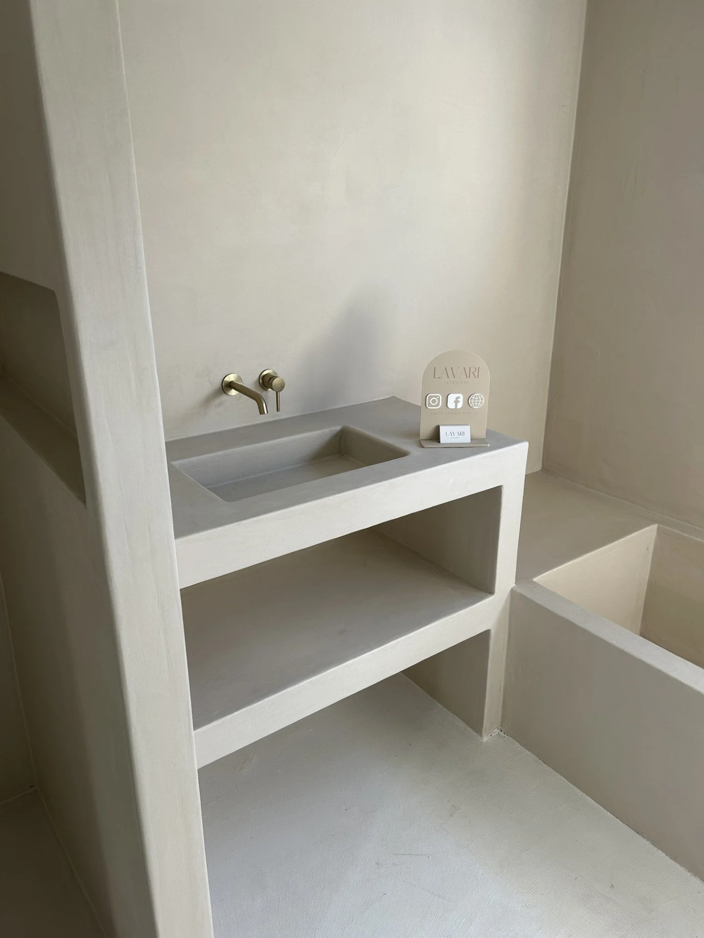Minimalist bathroom with concrete sink, white walls, and a small display sign with social media icons.