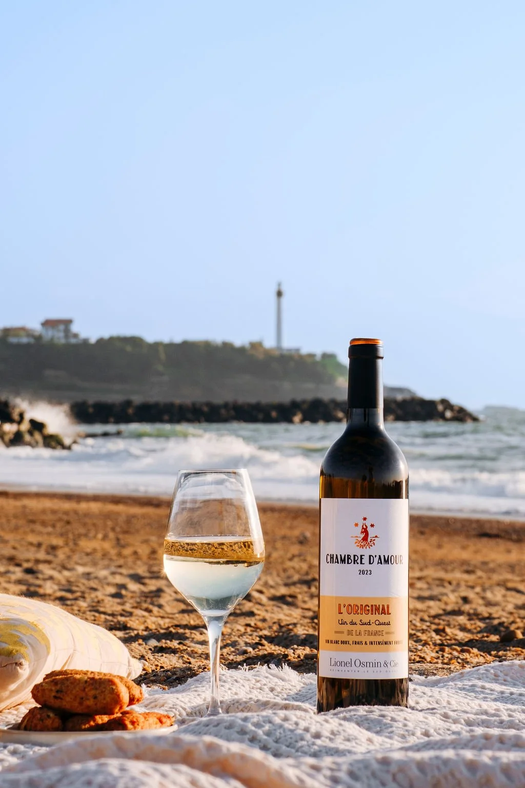 Bouteille de blanc sec Lionel Osmin posée sur le sable de la plage d'Anglet dans une ambiance lumineuse