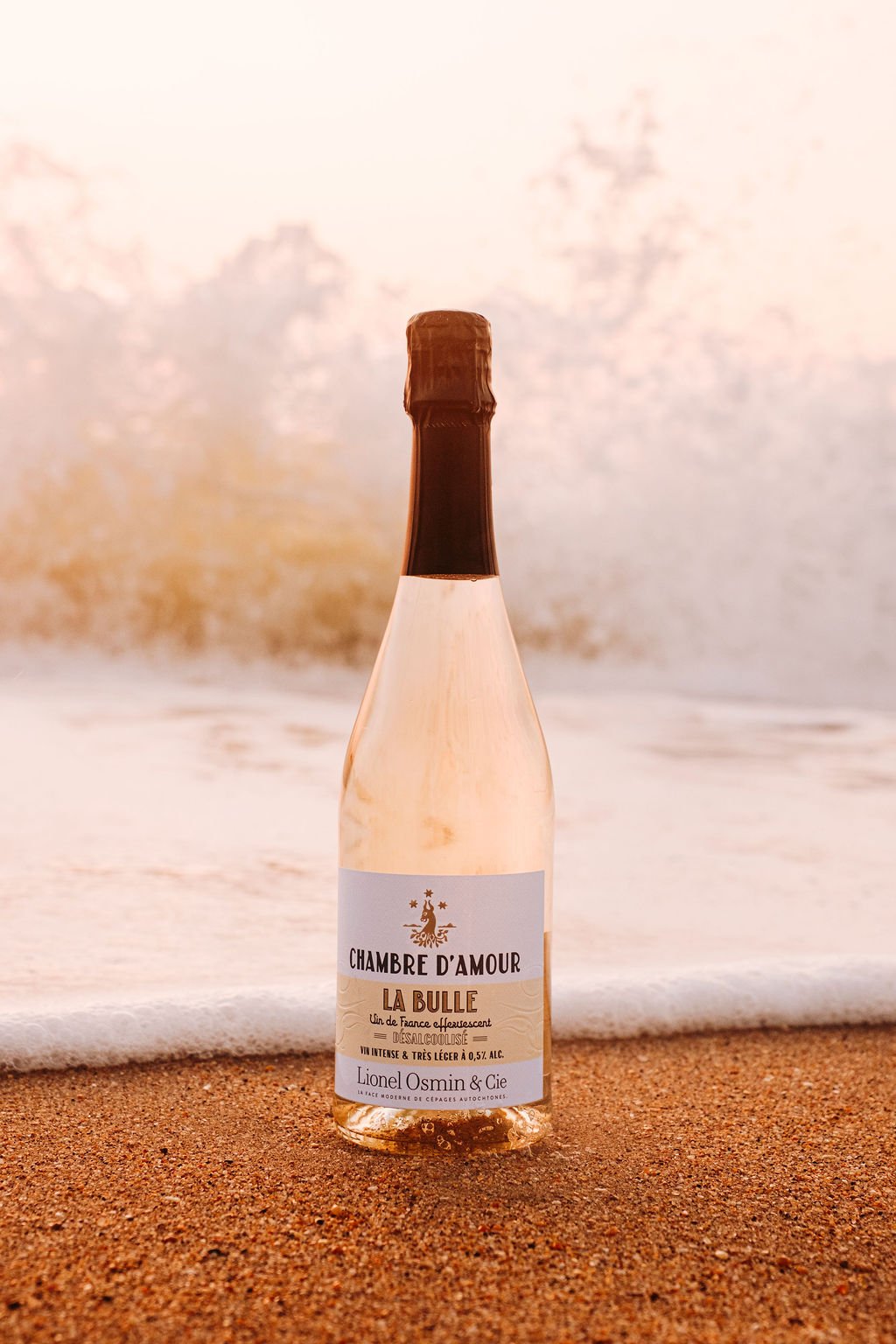 Bouteille de blanc doux Lionel Osmin posée au bord de l'océan au coucher du soleil près de Biarritz.