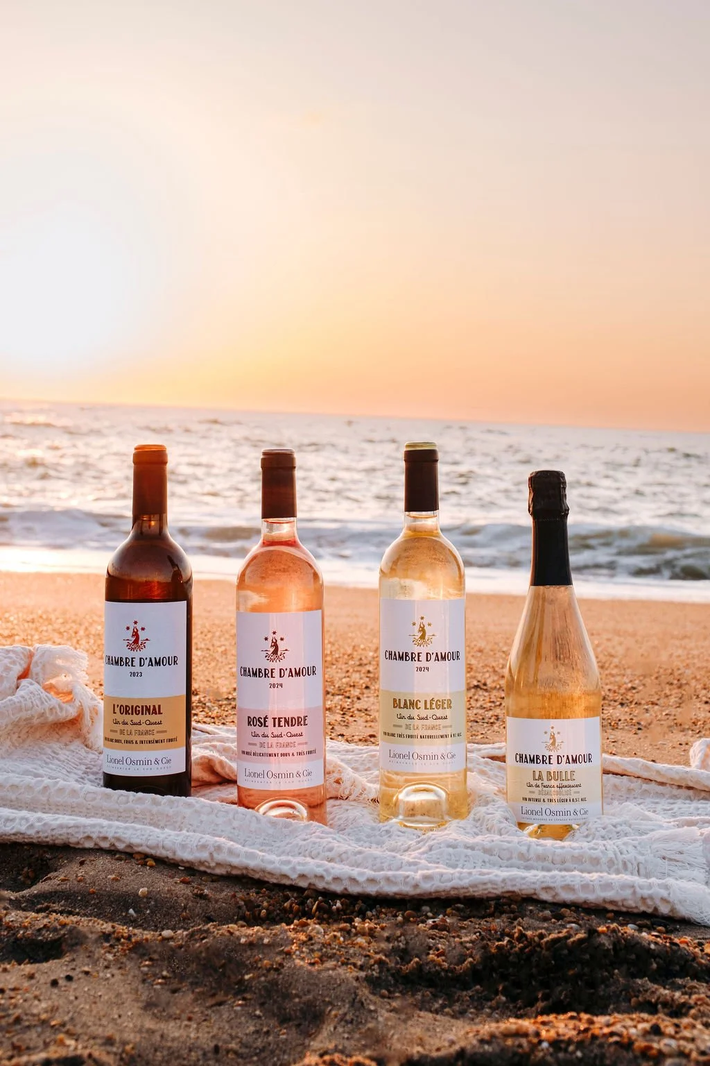 La gamme complète des 4 cuvées Lionel Osmin, incluant le sans alcool, alignées sur la plage de la Chambre d'Amour