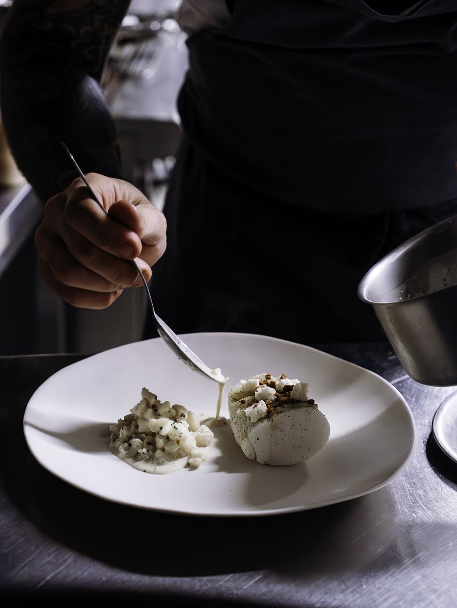 Geste précis du cuisinier versant une sauce sur un plat blanc en cuisine dans le 64