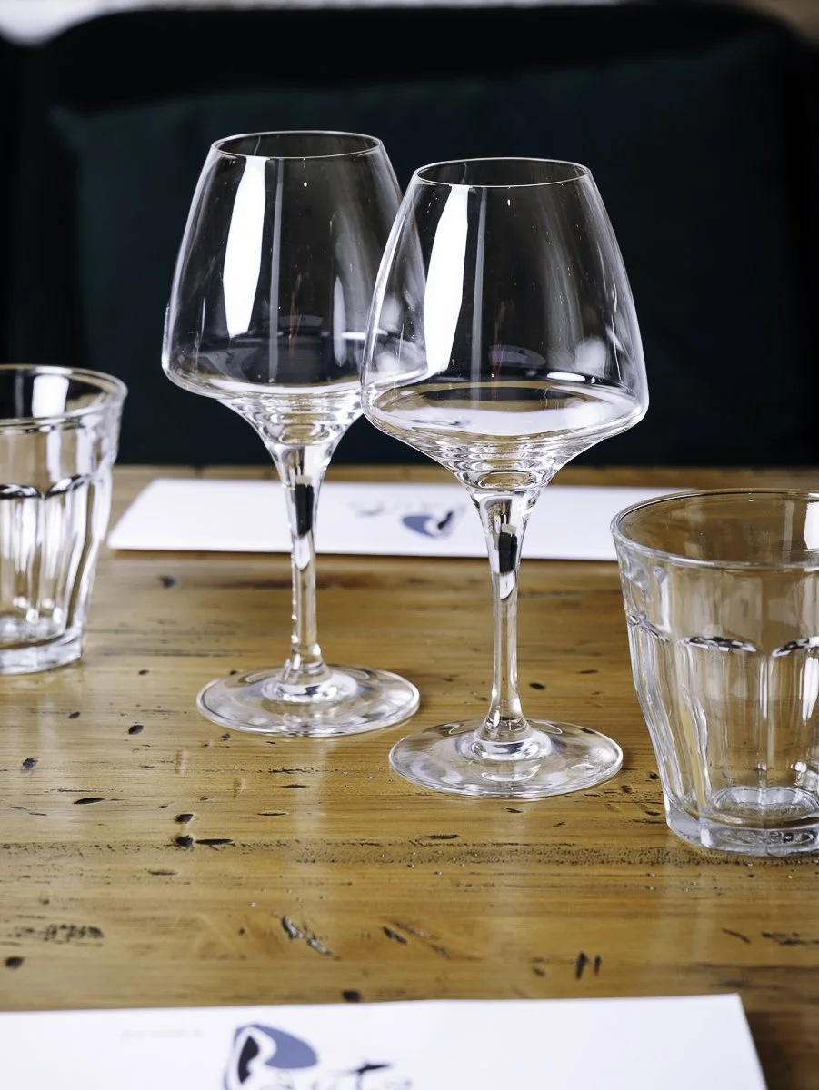 Verres à vin et verres d'eau dressés sur une table en bois clair