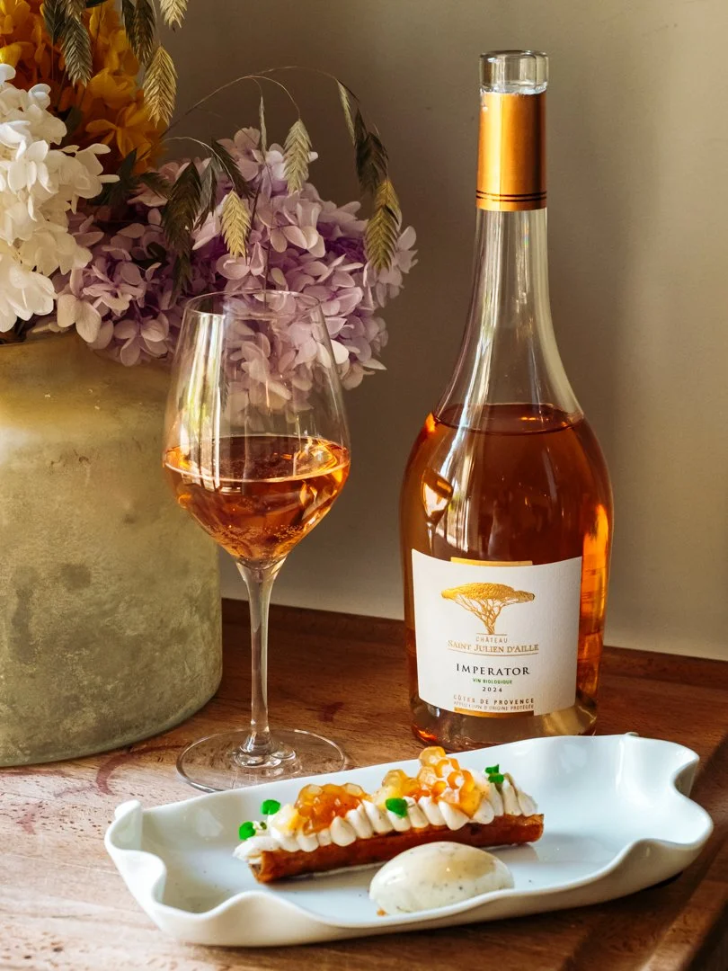 Bouteille de vin rosé Imperator avec verre et dessert fin sur une table en bois clair