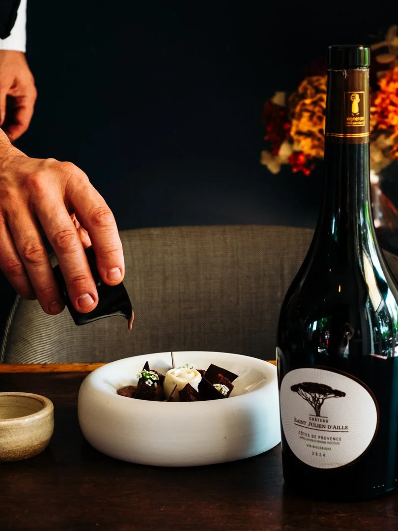 Main versant du chocolat sur un dessert à côté d'une bouteille de vin rouge