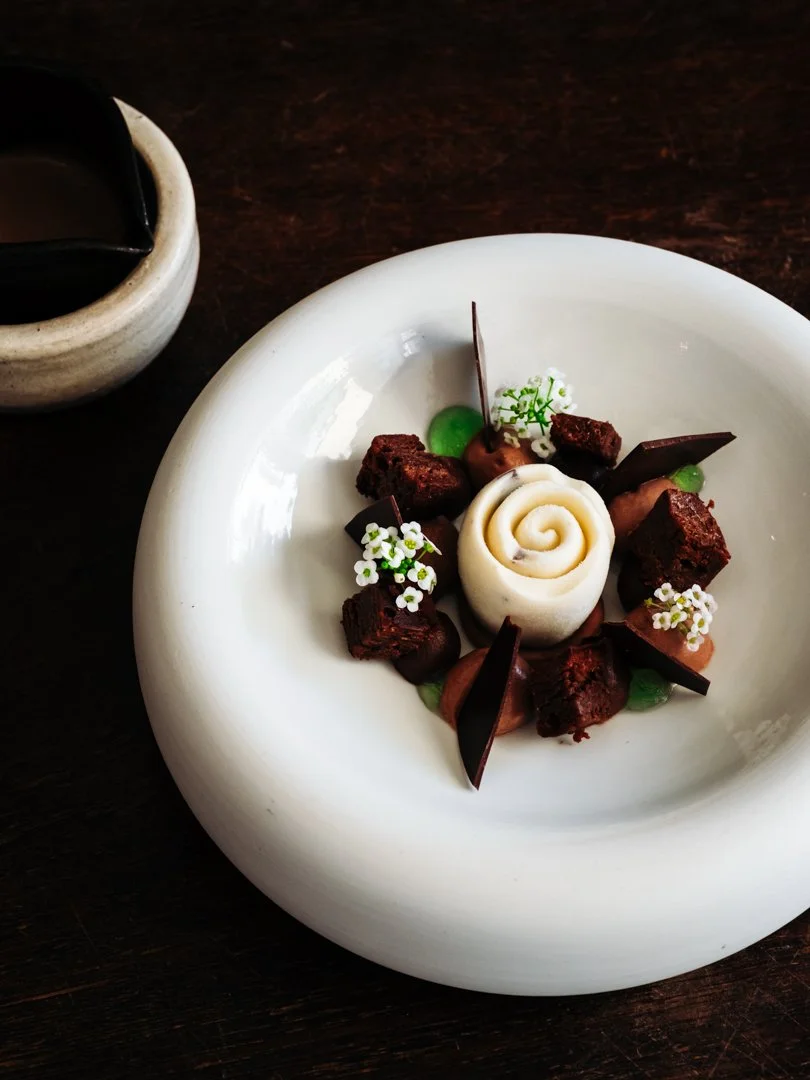 Dessert en forme de rose blanche entourée de brisures de chocolat sur une assiette creuse
