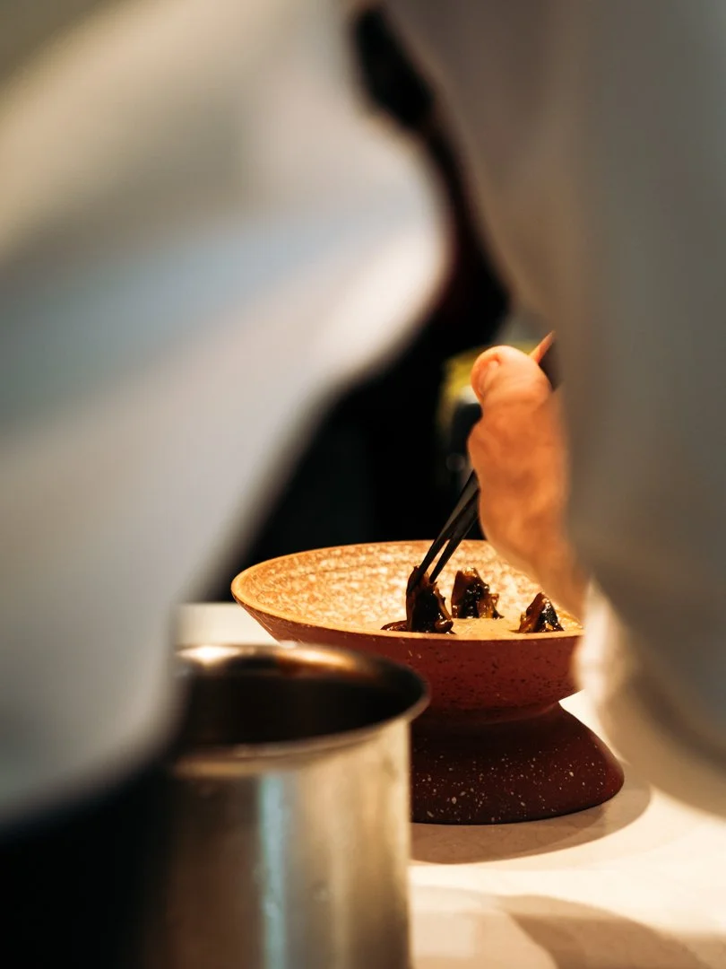 Main d'un cuisinier utilisant une pince de précision pour le dressage d'un plat créatif