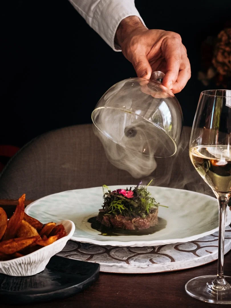 Main soulevant une cloche de fumage en verre pour un plat gastronomique à Saint-Pée-sur-Nivelle