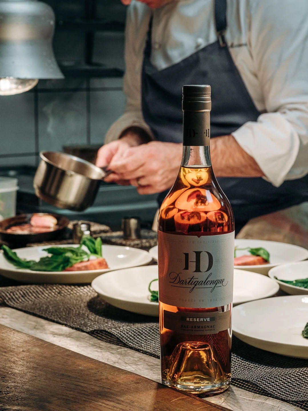 Bouteille Dartigalongue Réserve au premier plan, chef en cuisine