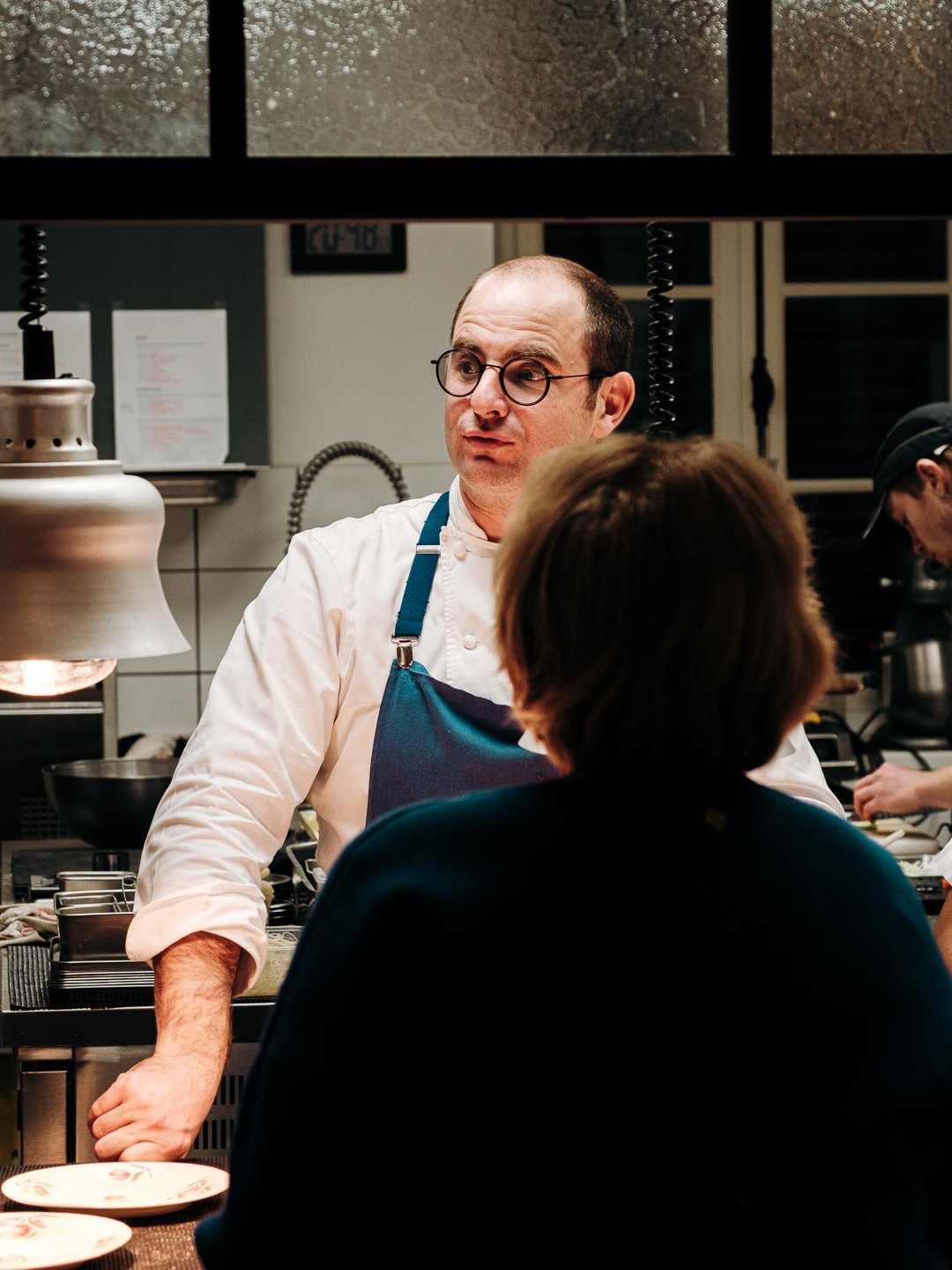 Chef Patxi Massonde échangeant avec une cliente depuis la cuisine ouverte, Mont Riant