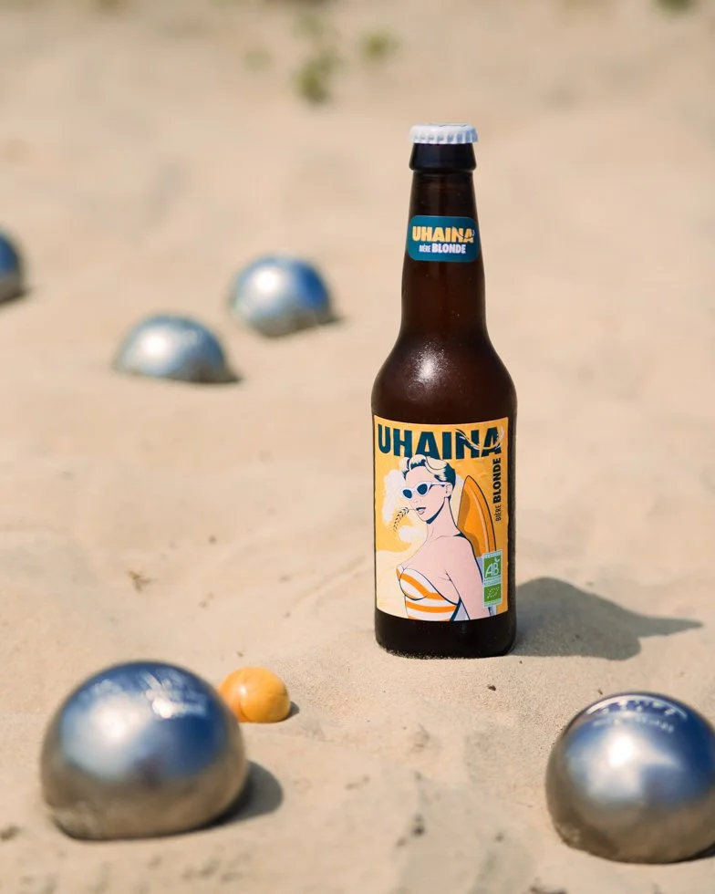 Bouteille Uhaina Blonde entourée de boules de pétanque sur une plage d'Hendaye