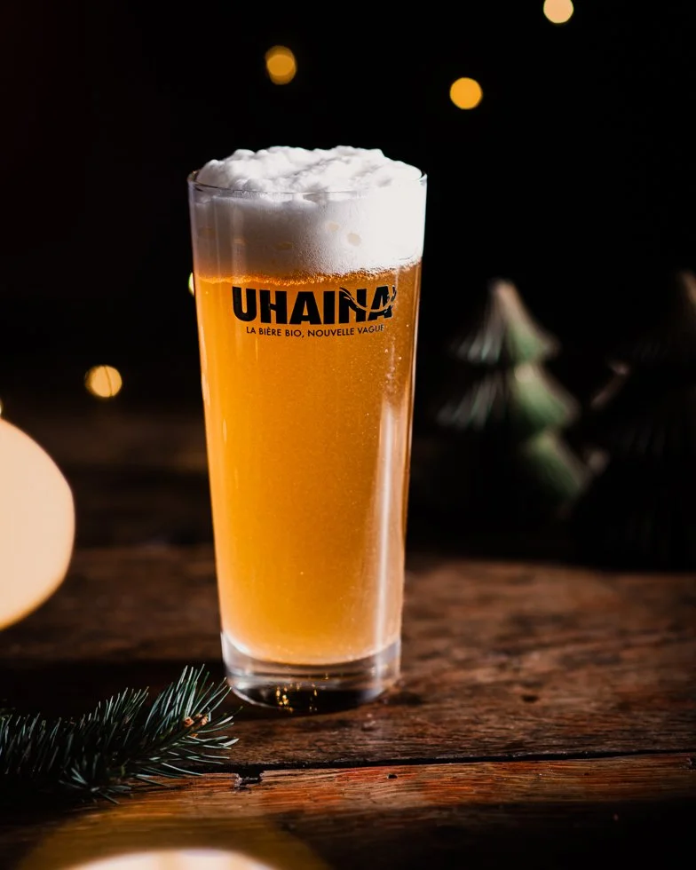 Verre Uhaina plein de mousse sur fond sombre, bokeh de Noël, photographie lifestyle bière