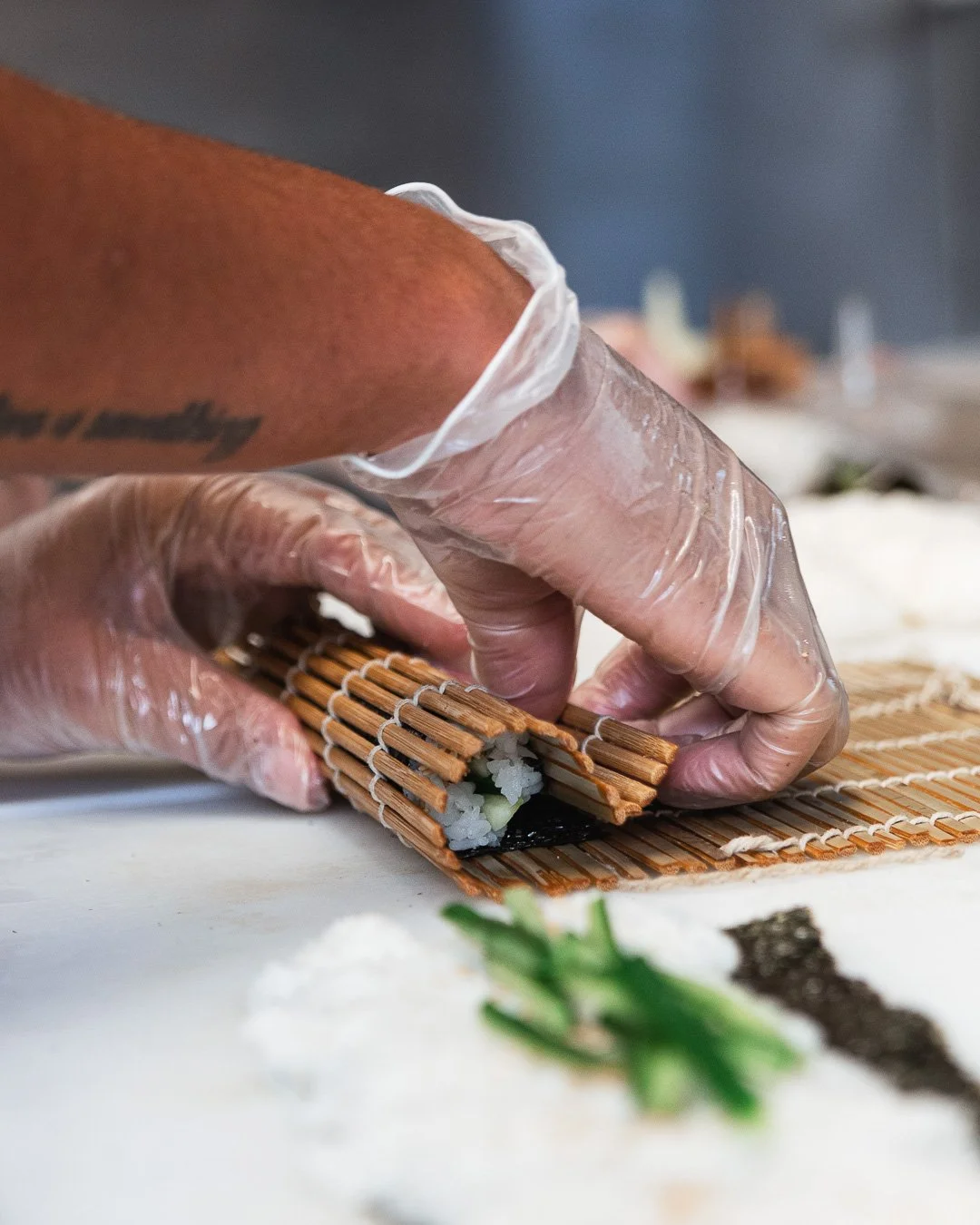 Mains gantées roulant un maki avec une natte en bambou, reportage métier cuisine
