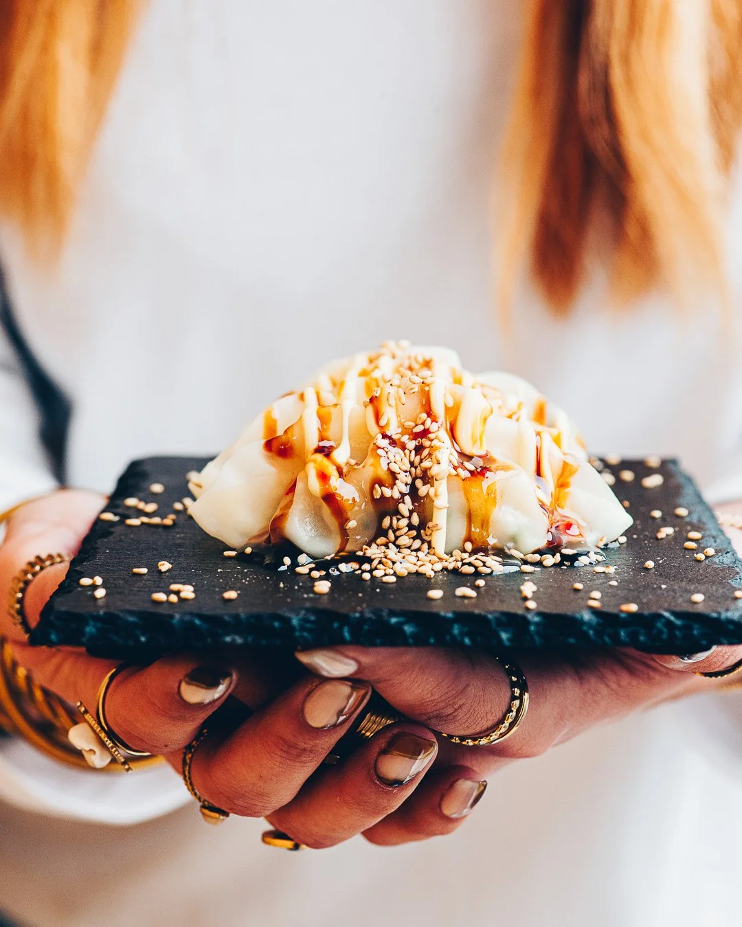 Mains tenant une ardoise avec un gyoza nappé de sauce et sésame, photographie culinaire Landes