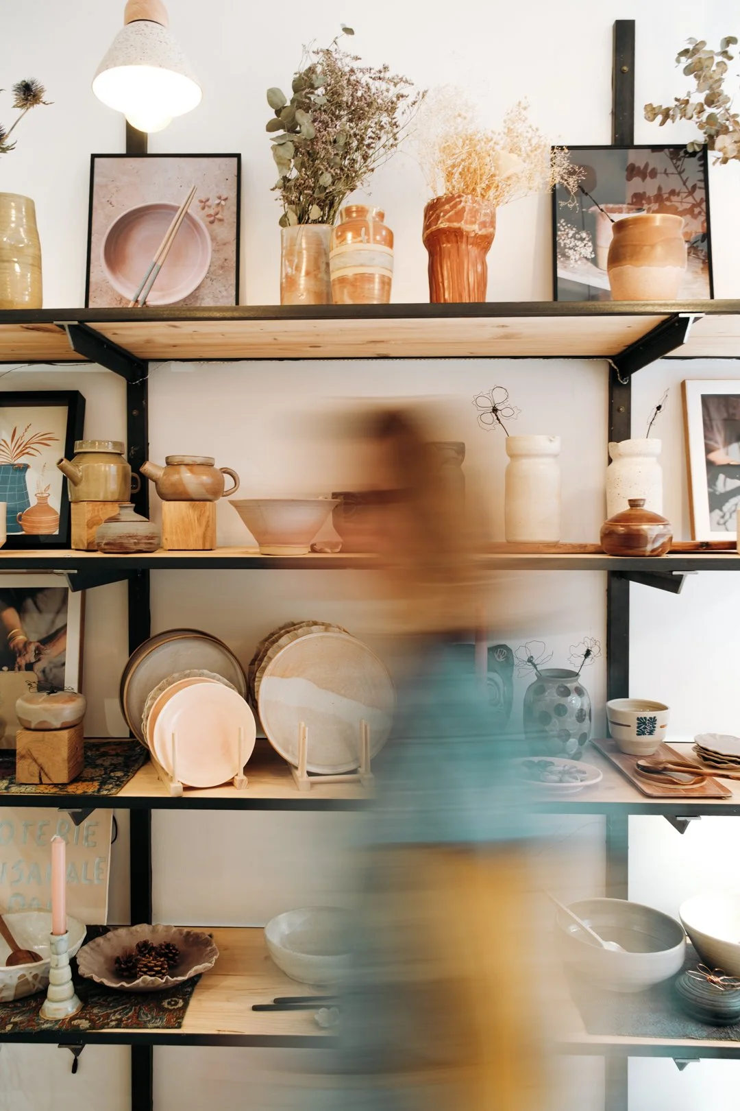 Intérieur lumineux de l'atelier Terre by NMP à Pau avec étagères de poteries et personne floue