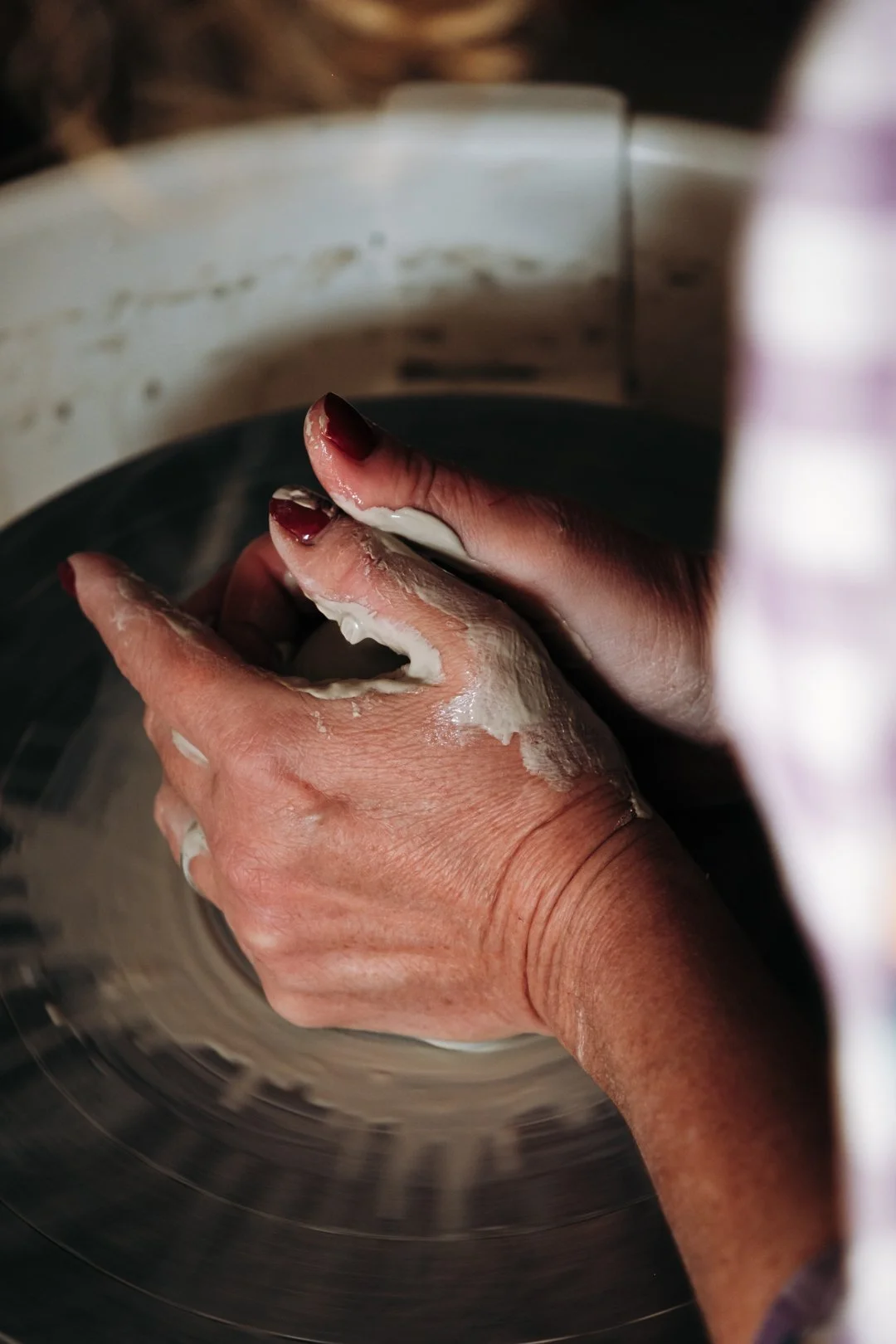 Très gros plan sur les mains d'une céramiste avec vernis rouge façonnant la terre sur le tour, reportage métier potière à Pau