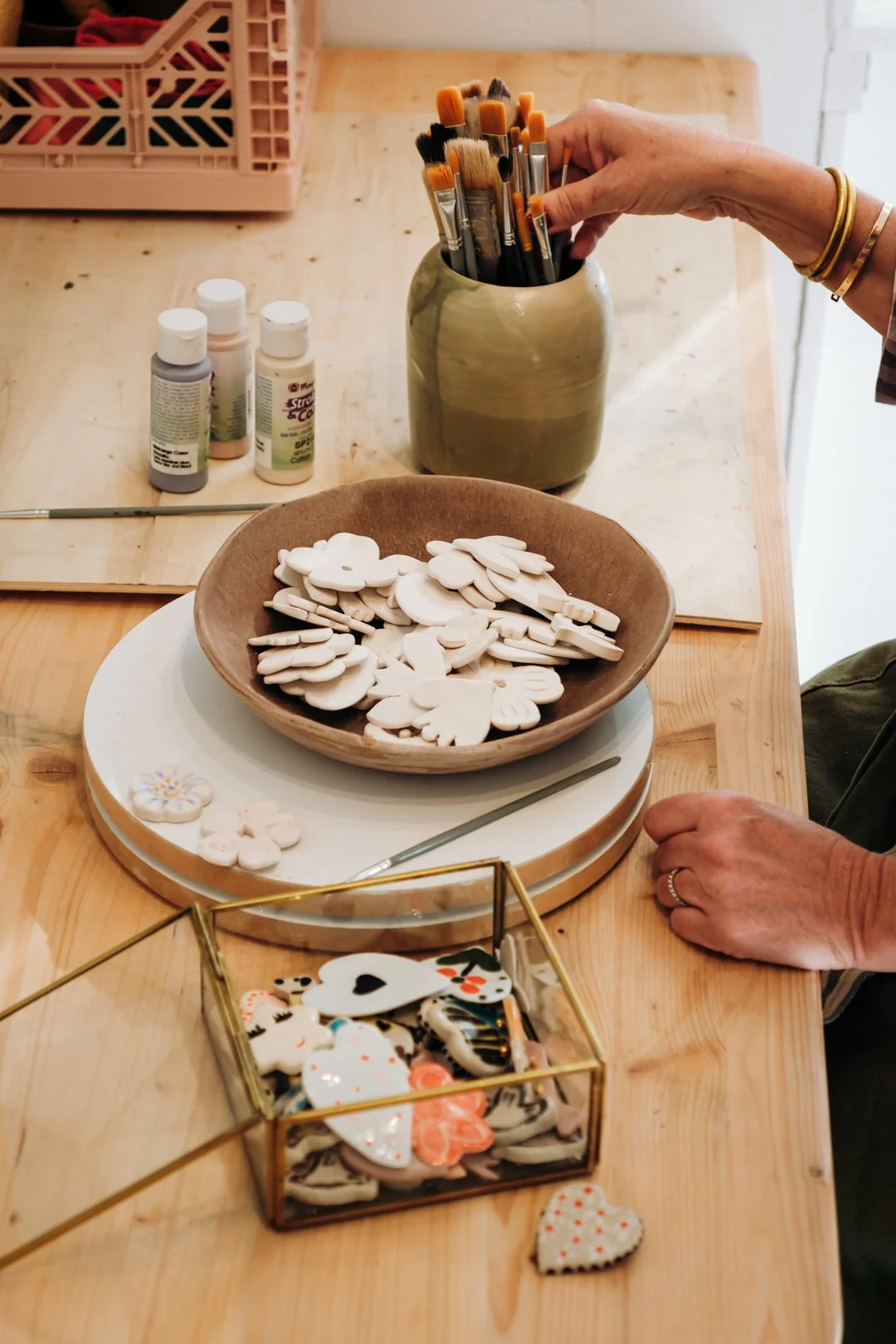 Plan moyen sur des pinceaux dans un pot et des petites pièces céramiques en forme de fleurs, photographie d'artisanat à Pau