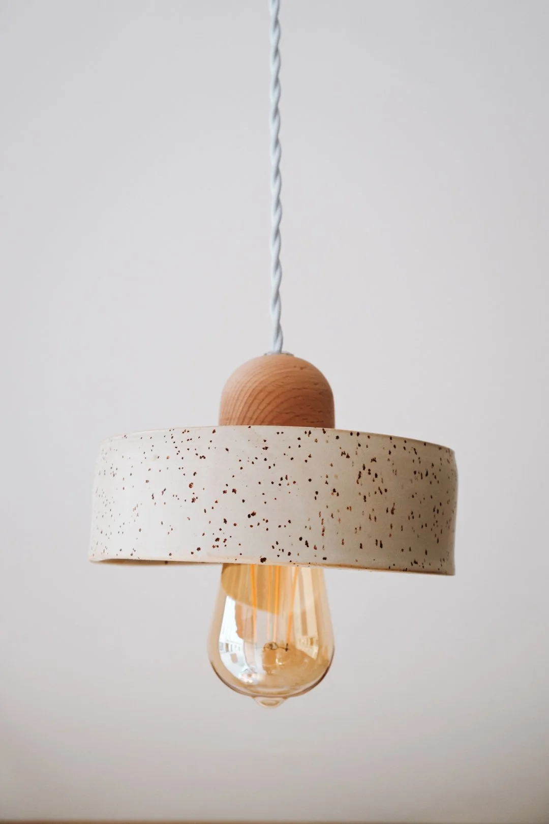 Gros plan sur un luminaire suspendu avec abat-jour en céramique mouchetée et bois, photographie de céramique