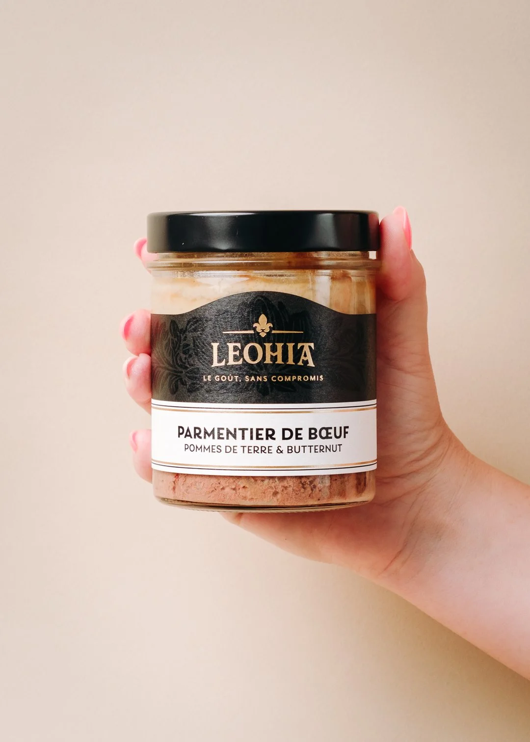 Main avec vernis rose tenant un bocal de Parmentier de Bœuf pommes de terre et butternut Leohia sur fond studio, photographie de produits food
