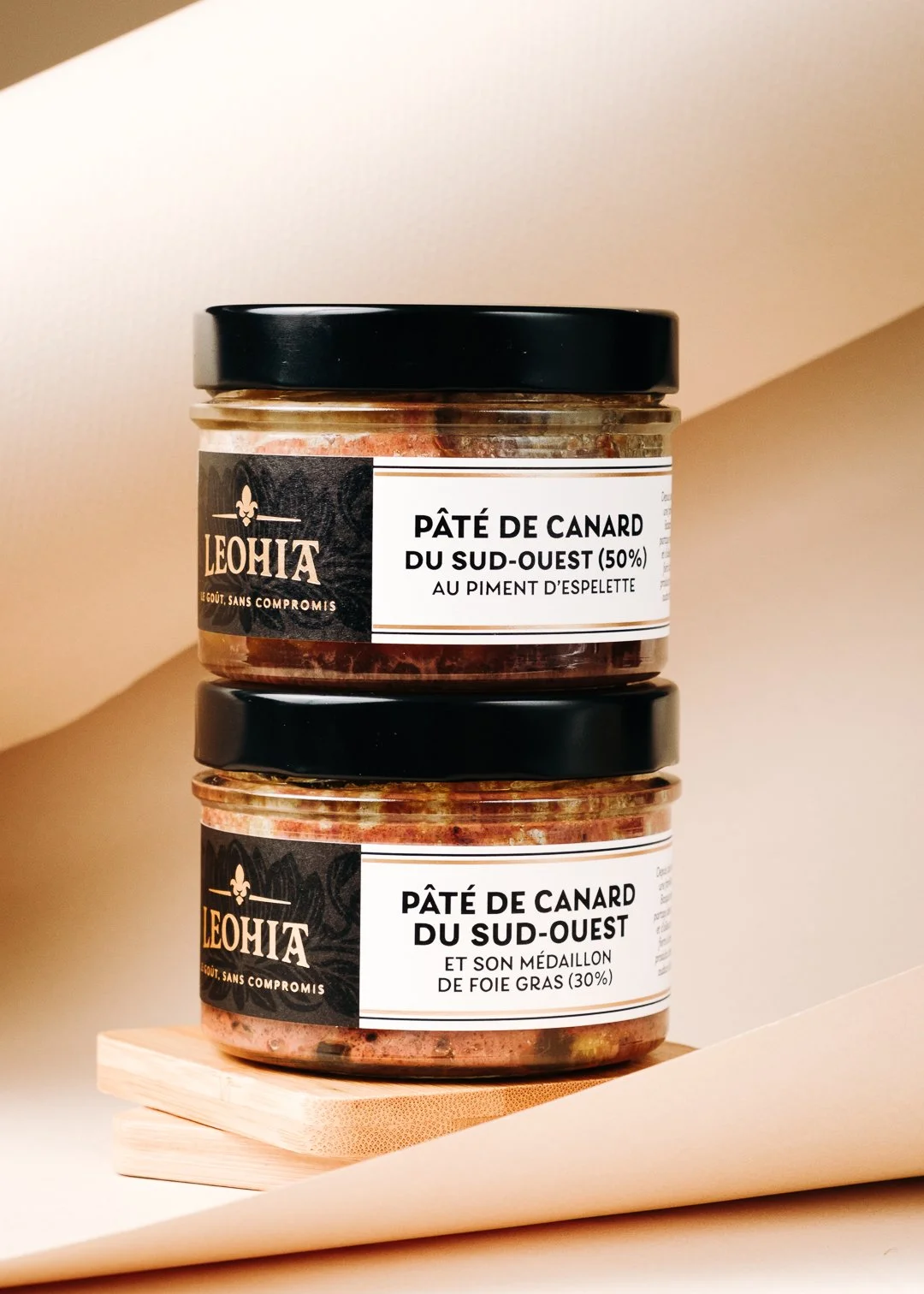 Pile graphique de deux bocaux Leohia de Pâté de Canard sur fond studio beige épuré, packshot premium Pays Basque