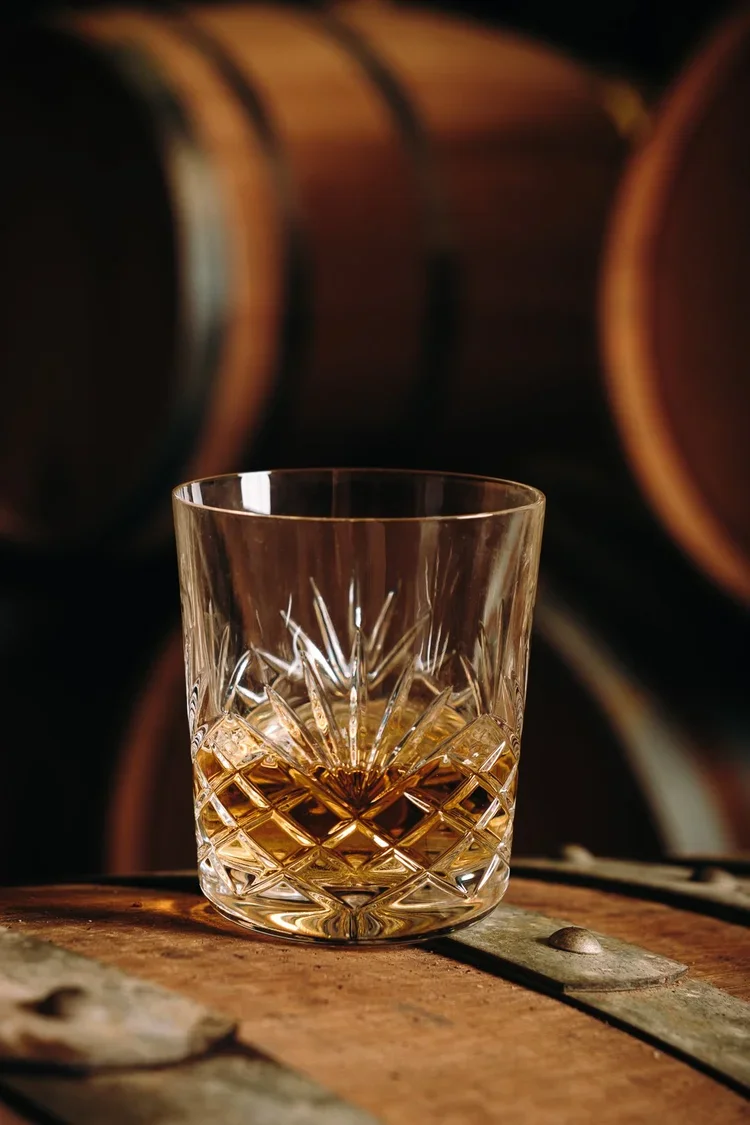 Verre de whisky taillé posé sur un tonneau en bois, photographie de spiritueux Domaine Brana au Pays Basque