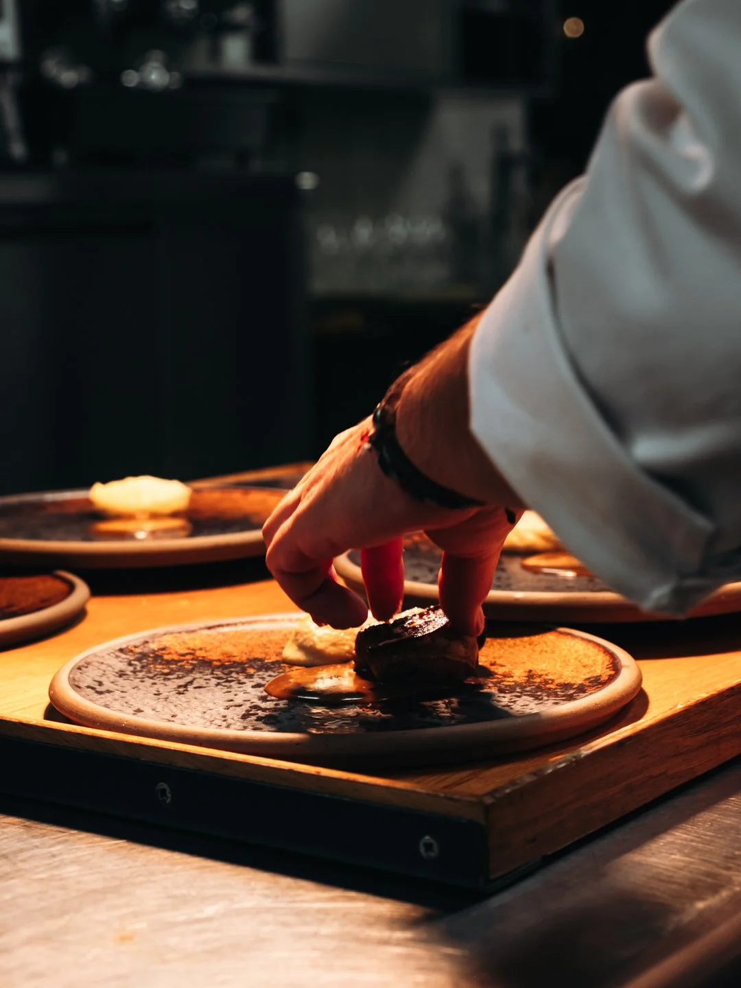 Main dressant une assiette sombre sur plateau bois sous lumiere chaude, service gastronomique.