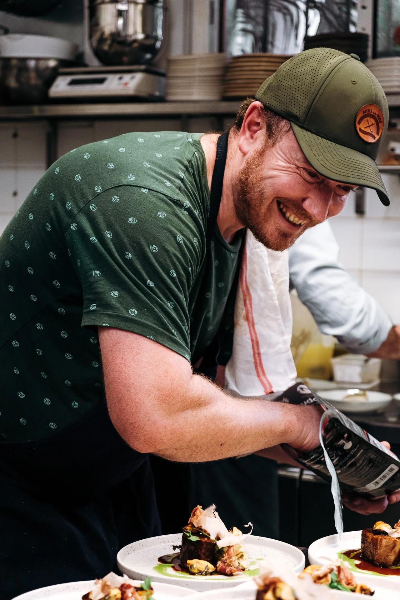 Chef souriant versant une sauce sur des assiettes lors du diner 7 ans 7 chefs au Snug a Pau.