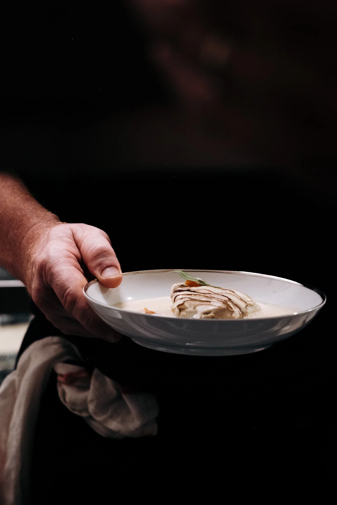 Main tenant une assiette blanche avec preparation gastronomique, service soiree au Snug.