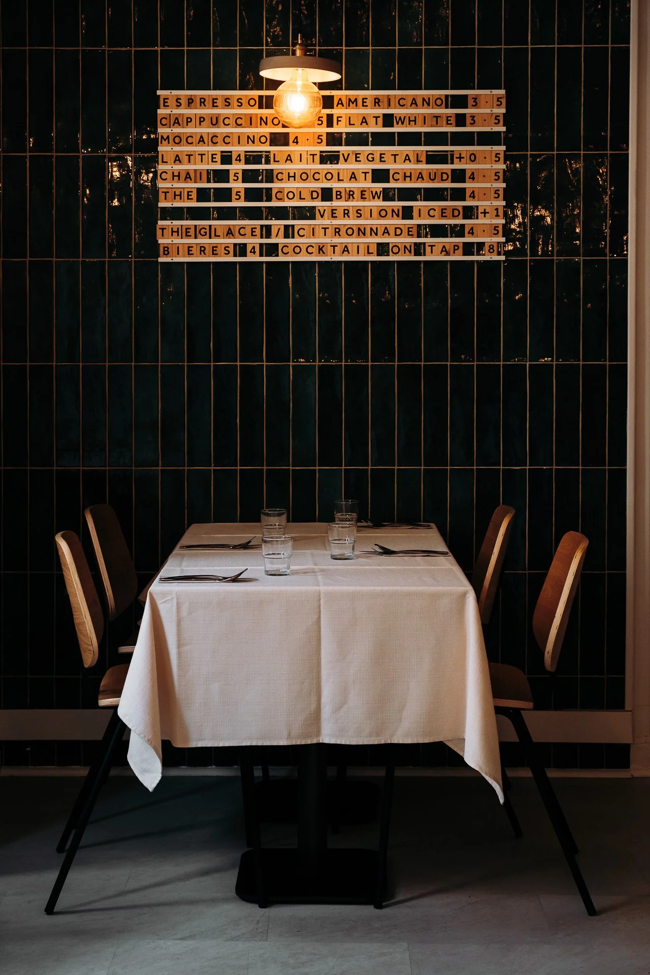 Table dressee avec nappe blanche devant le carrelage vert du Snug bar a Pau.