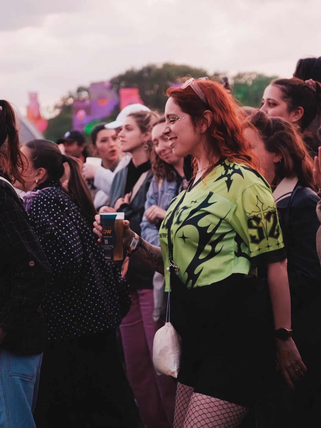 Festivaliere souriante et dansant en tenue coloree dans la foule au crepuscule, ambiance We Love Green