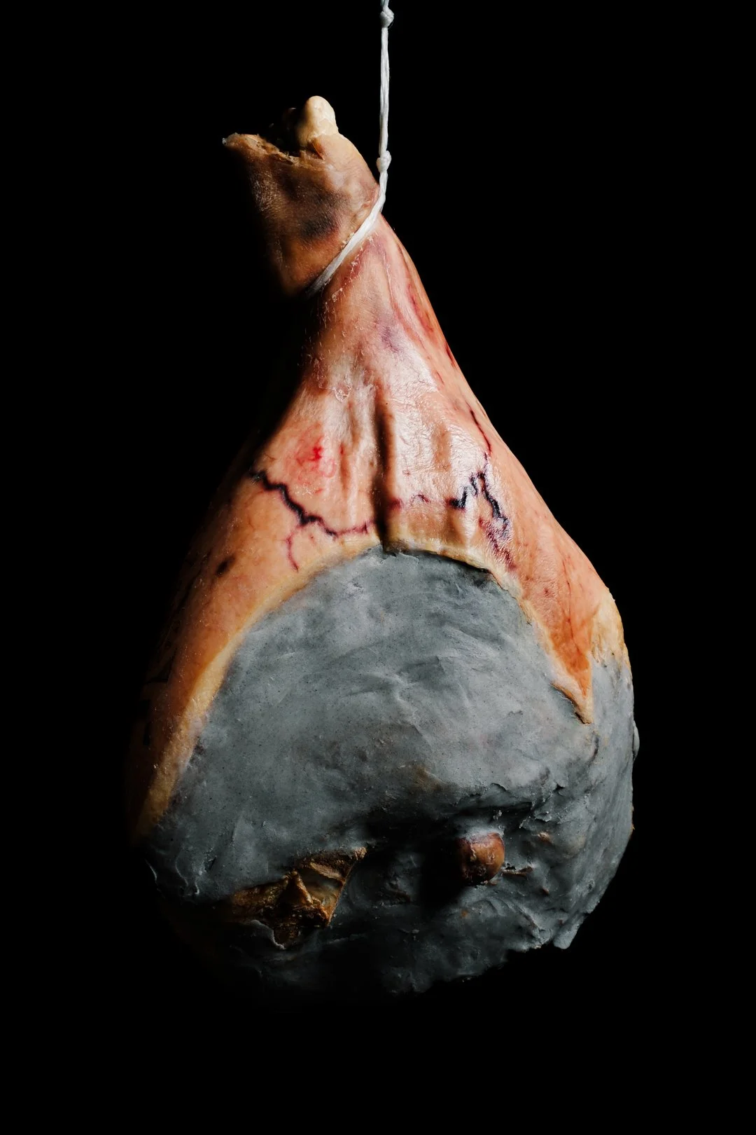 Pièce de jambon entier suspendue par une ficelle sur fond noir, style pour images épurées