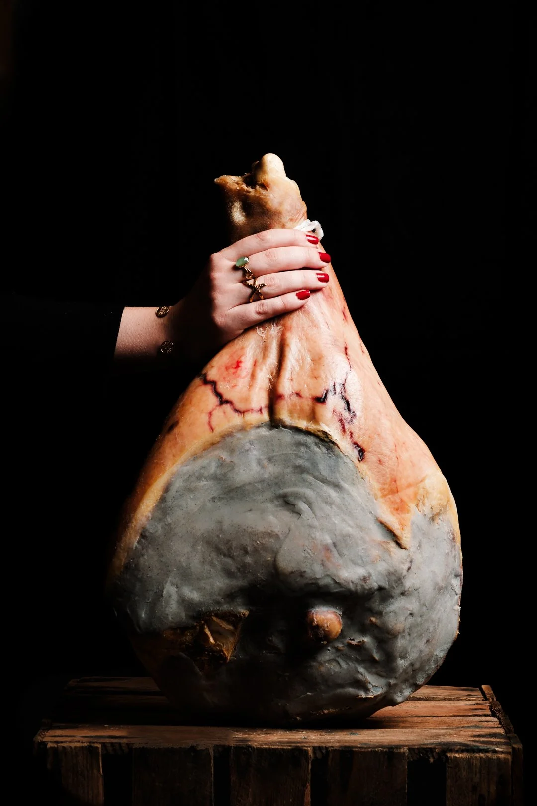 Main tenant une pièce entière de jambon à l'os sur fond sombre, photographie produit de terroir