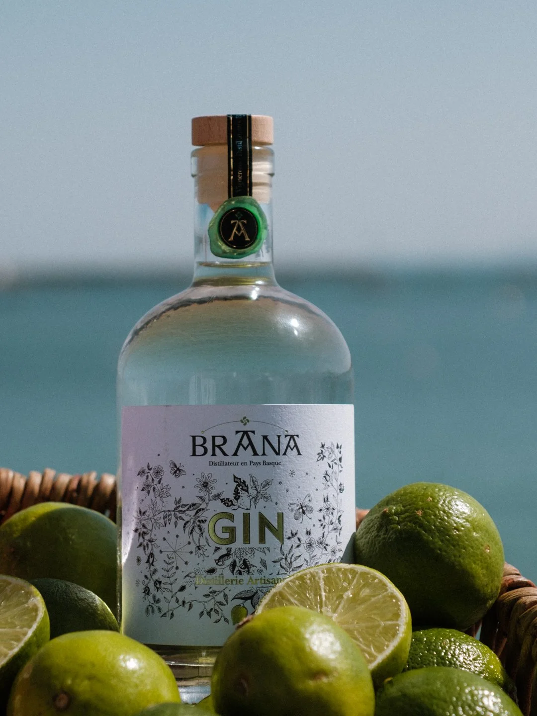Bouteille de Gin Brana entourée de citrons verts frais avec l'océan en arrière-plan