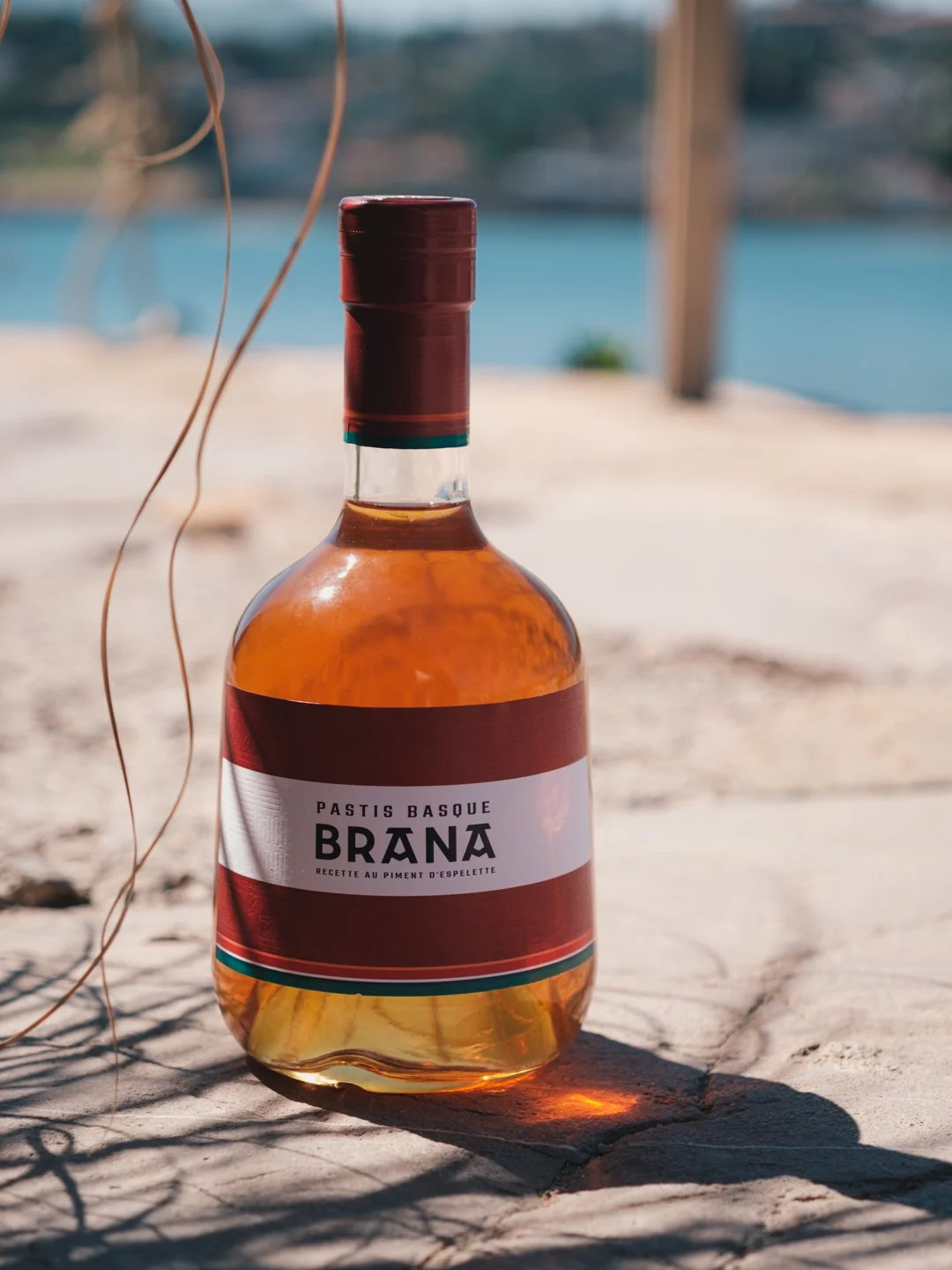 Bouteille de Pastis Basque traversée par la lumière crue de l'été sur un sol en pierre