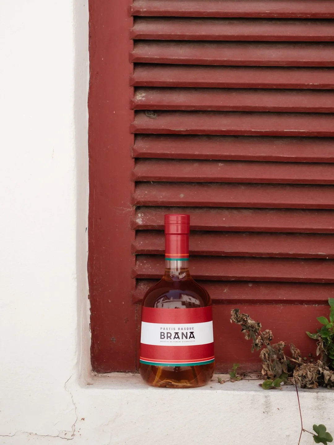 Le Pastis Basque Brana mis en avant devant des volets rouges traditionnels