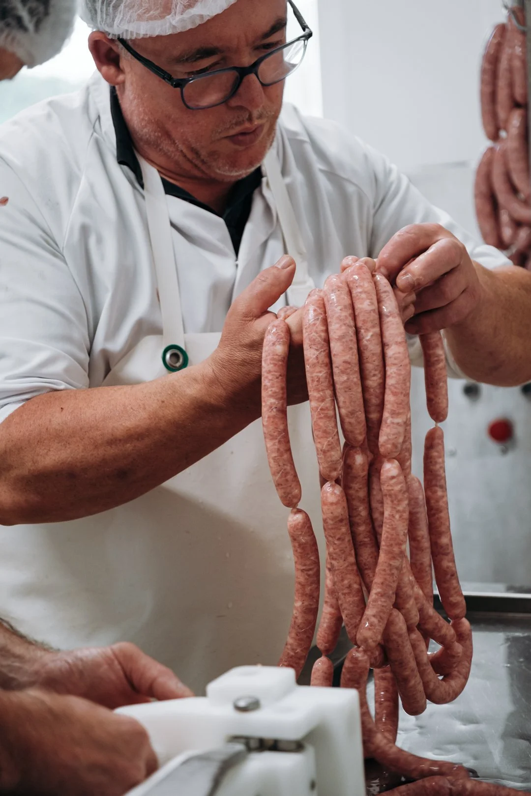 Charcutier en tenue de travail manipulant des brassées de saucisses fraîches dans le laboratoire de Villefranque