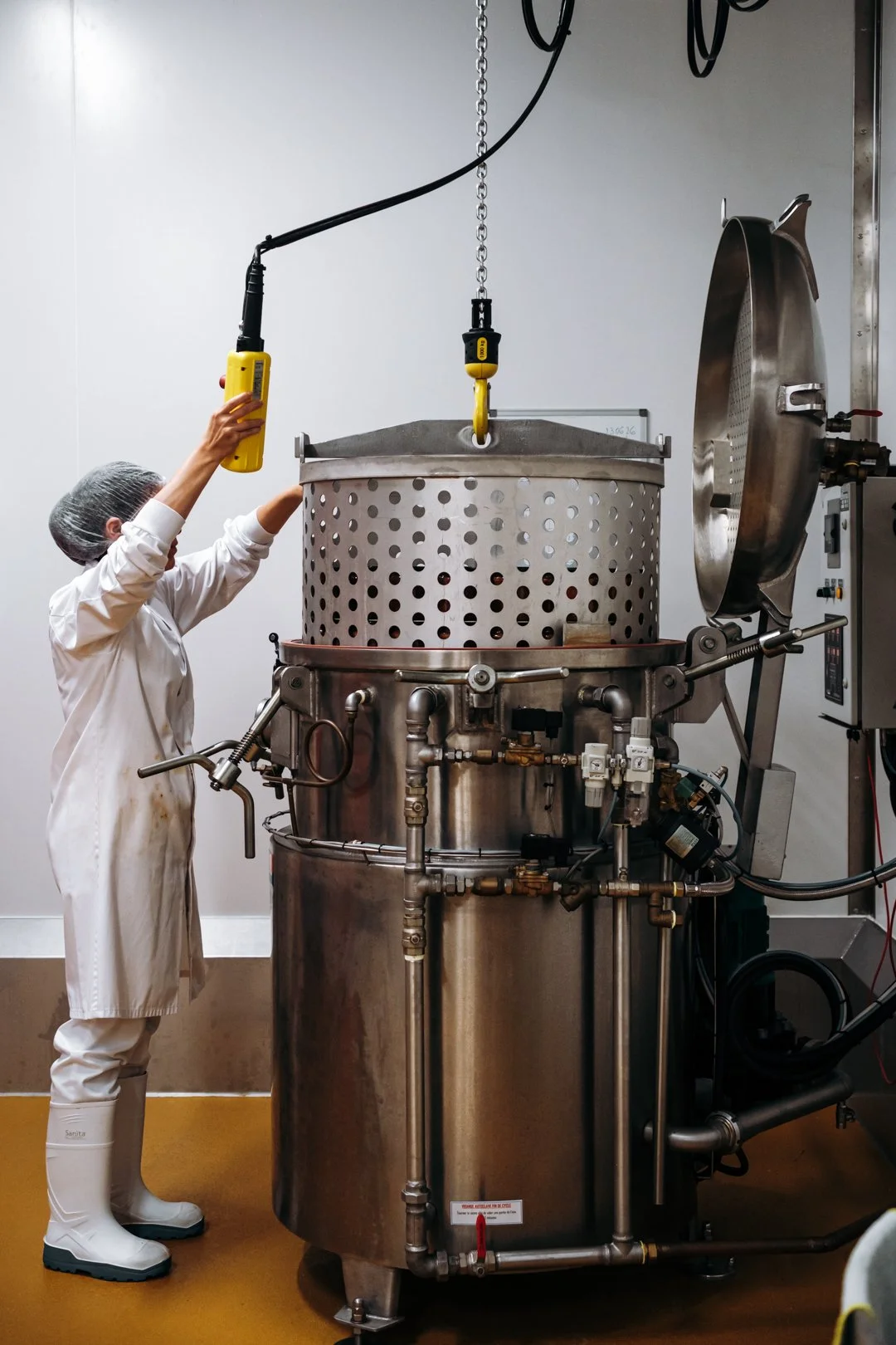 Opératrice utilisant un palan industriel pour plonger un panier entier de bocaux dans l'autoclave