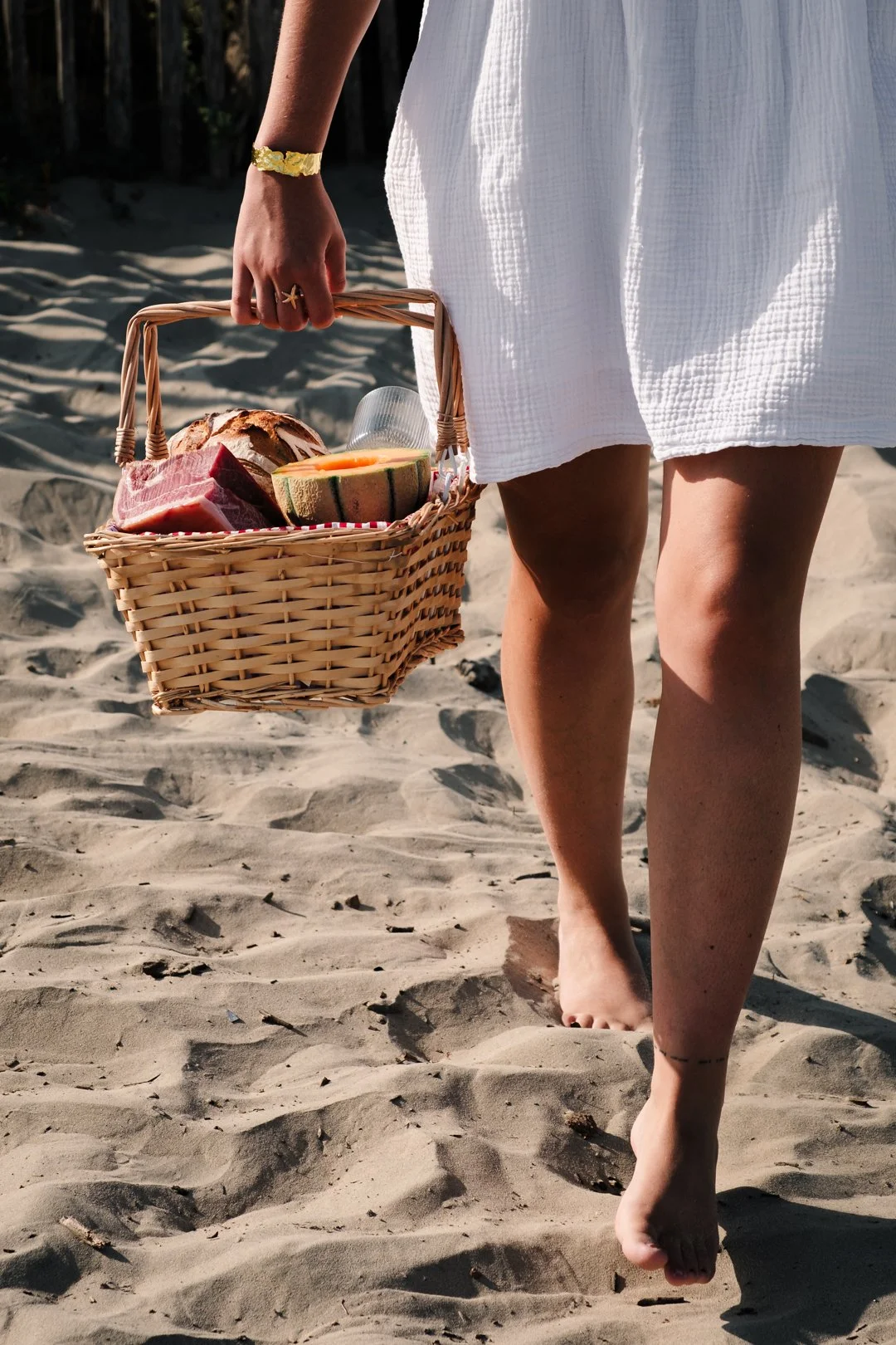 Femme portant un panier de pique-nique avec du jambon et un melon sur le sable à Saint-Jean-de-Luz
