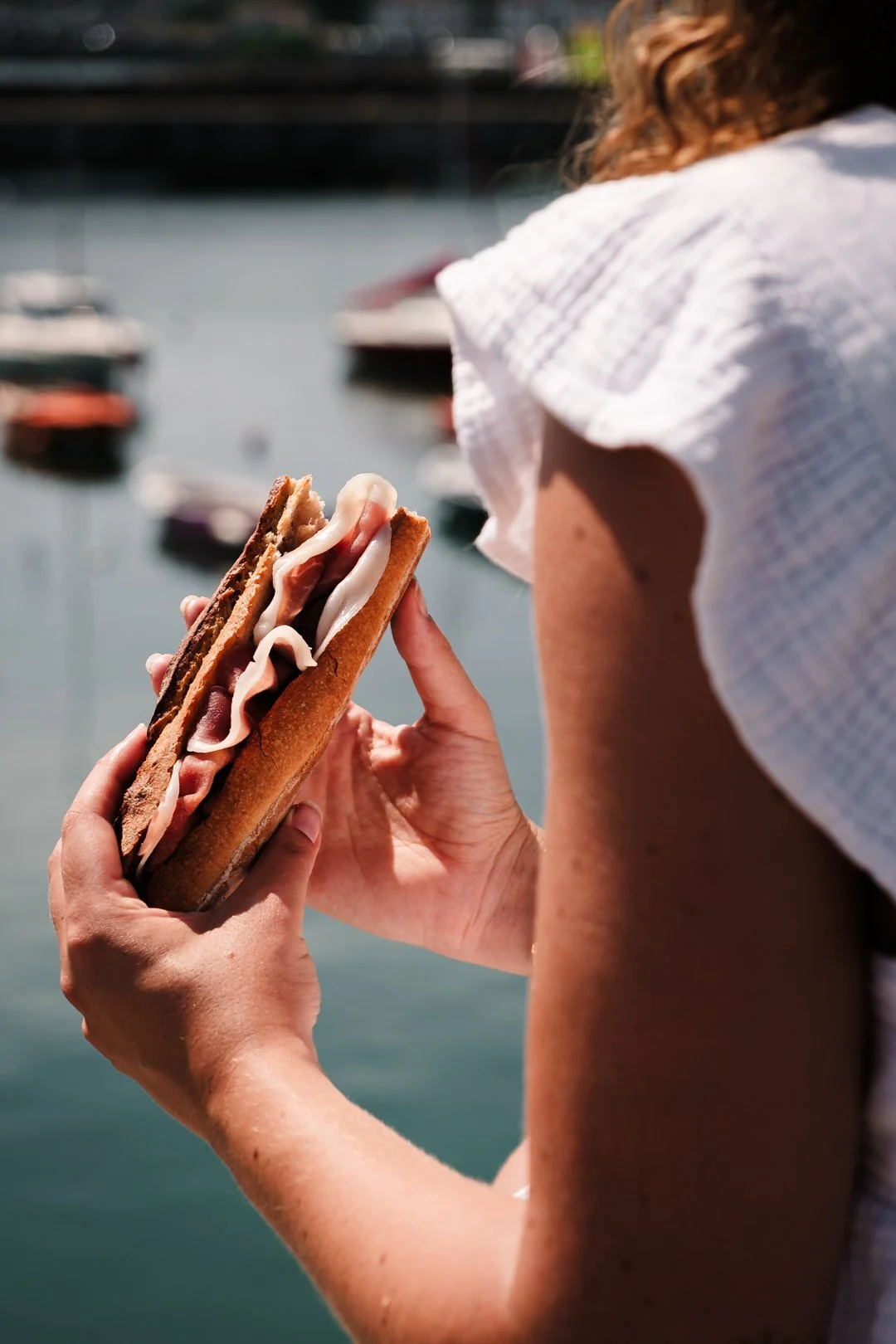 Sandwich baguette garni de jambon de Bayonne tenu face aux bateaux du port de Socoa