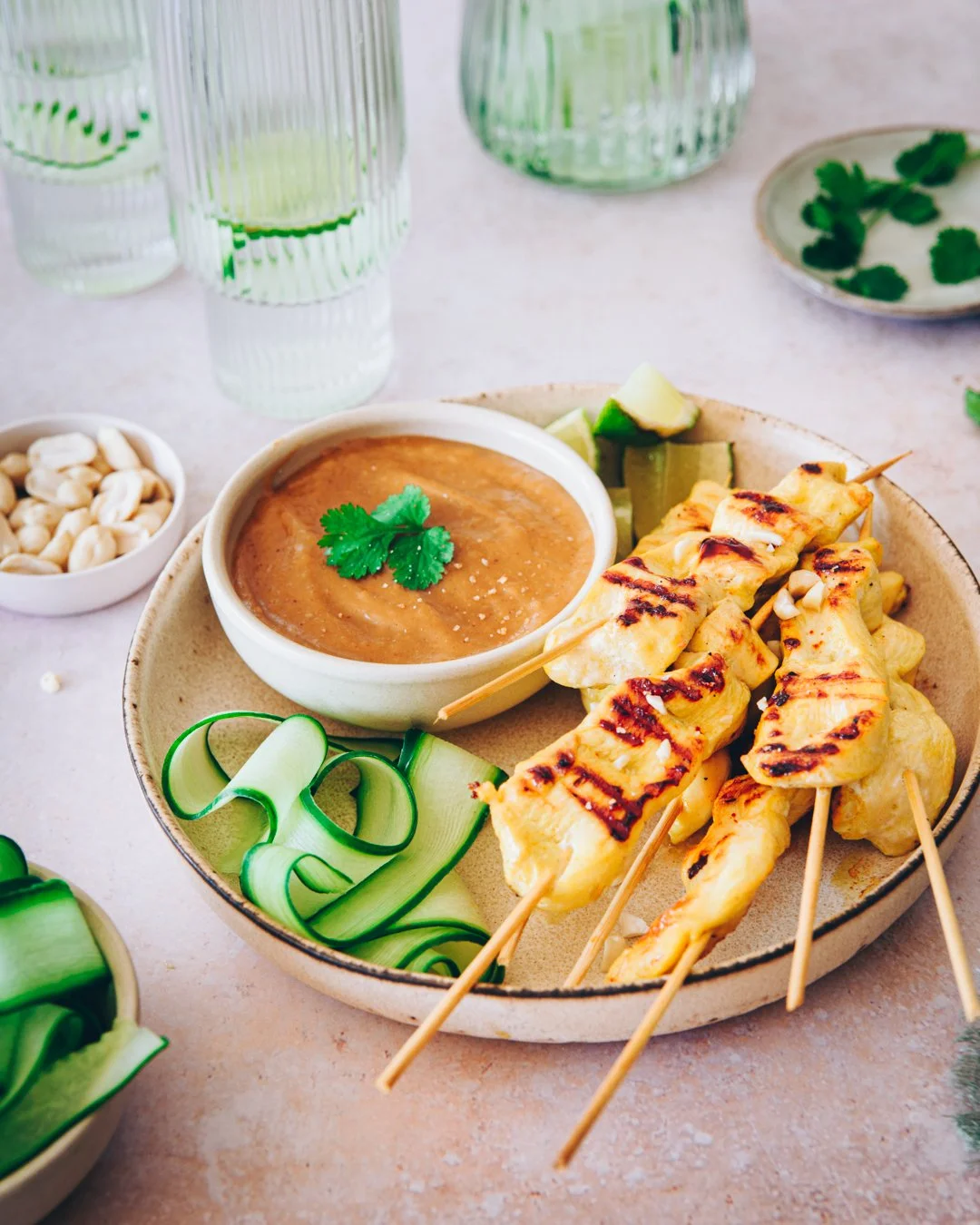 Brochettes de poulet satay grillées servies avec une sauce cacahuète et des lamelles de concombre.