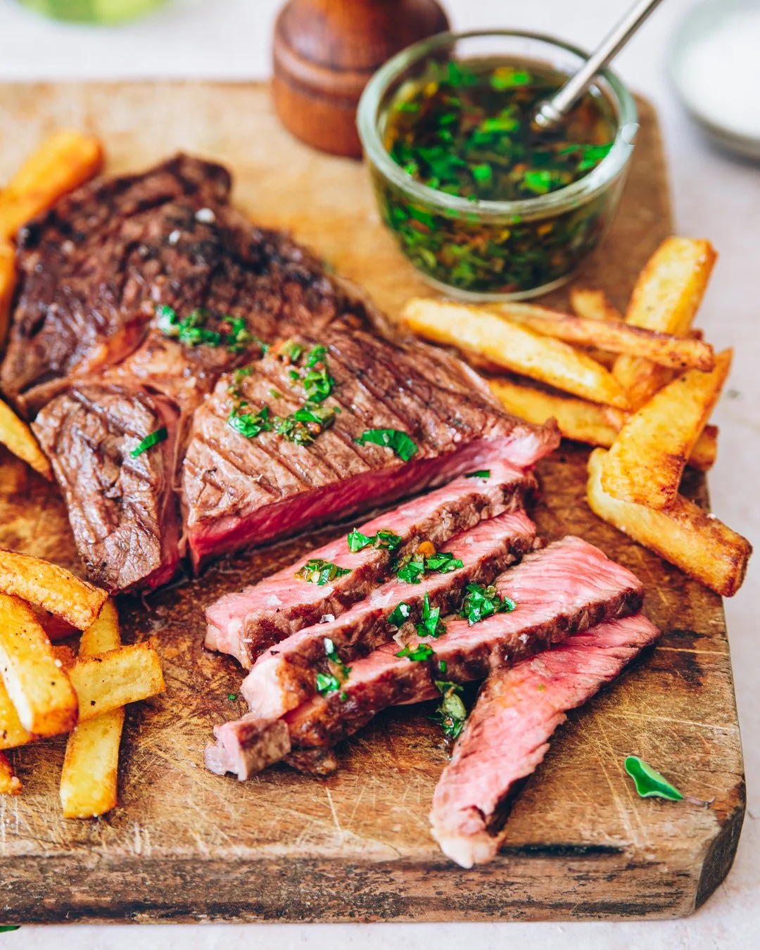 photo culinaire Entrecôte grillée tranchée servie sur planche en bois avec frites maison et sauce chimichurri