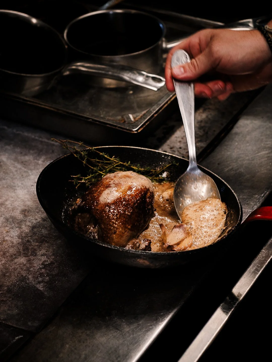 Main arrosant une volaille en cocotte fonte avec beurre mousseux, cuisine gastronomique Pau.