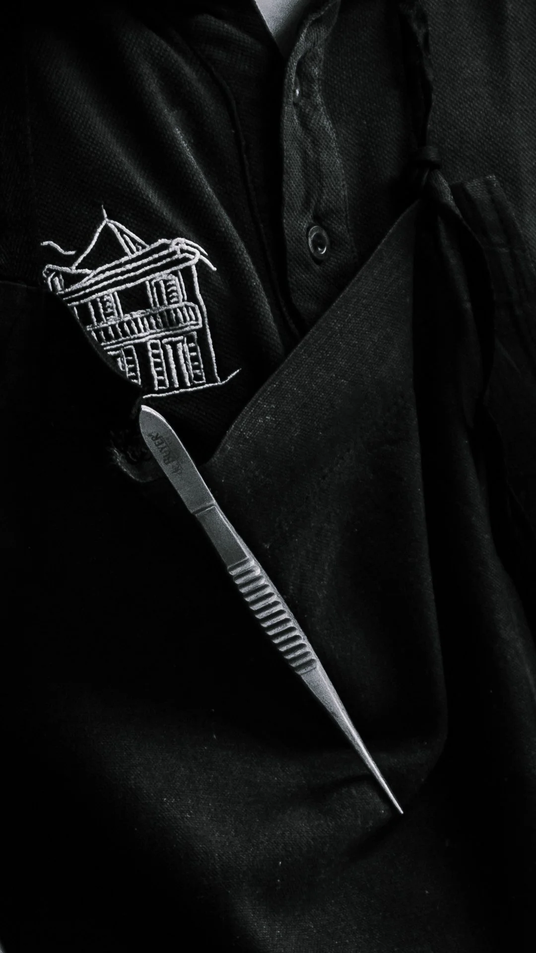 Detail veste de chef avec broderie logo l'Esberit et pince a dresser, noir et blanc.
