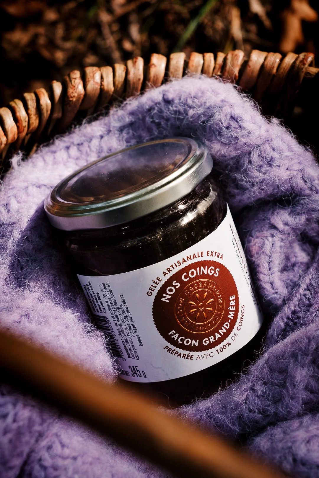 Pot de gelée de coings dans un panier en osier garni d’un tricot violet