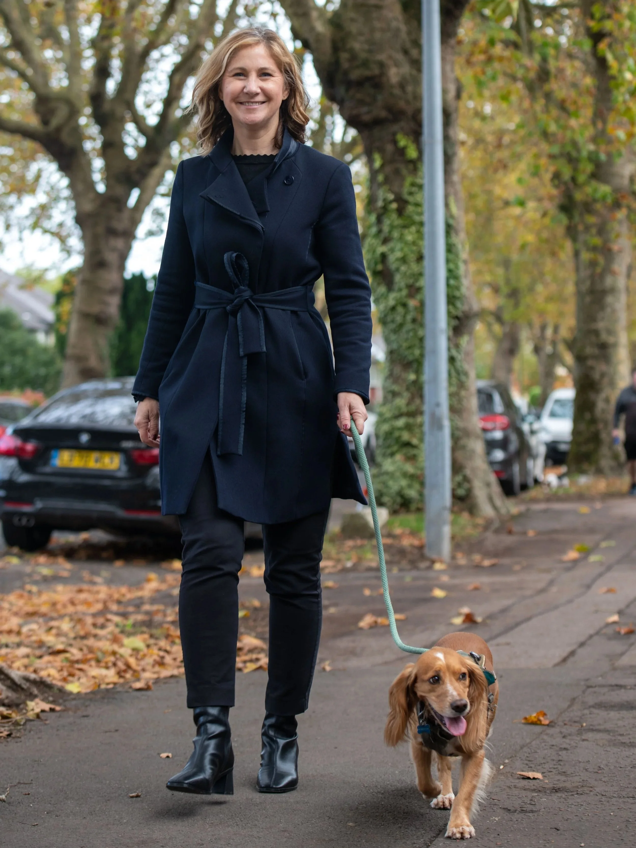 Anna McMorrin MP walking her dog, Cadi, with trees and cars in the background.