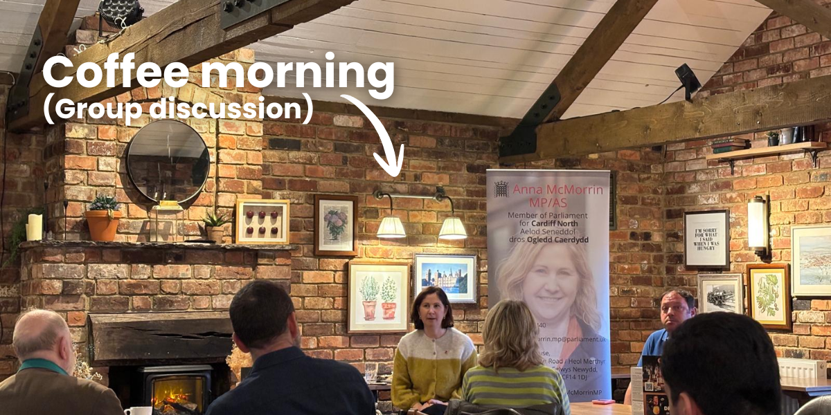 Anna McMorrin MP hosting a coffee morning at a restaurant with a brick interior. Several people are seated and listening.