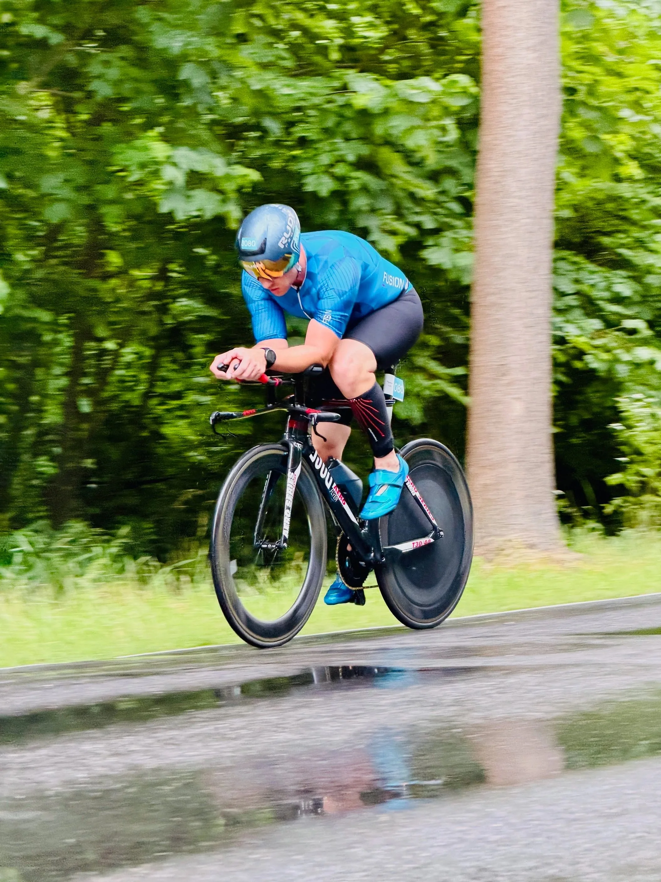 Ein Radfahrer in blauer Kleidung und Helm fährt auf einer Straße durch einen grünen Wald.