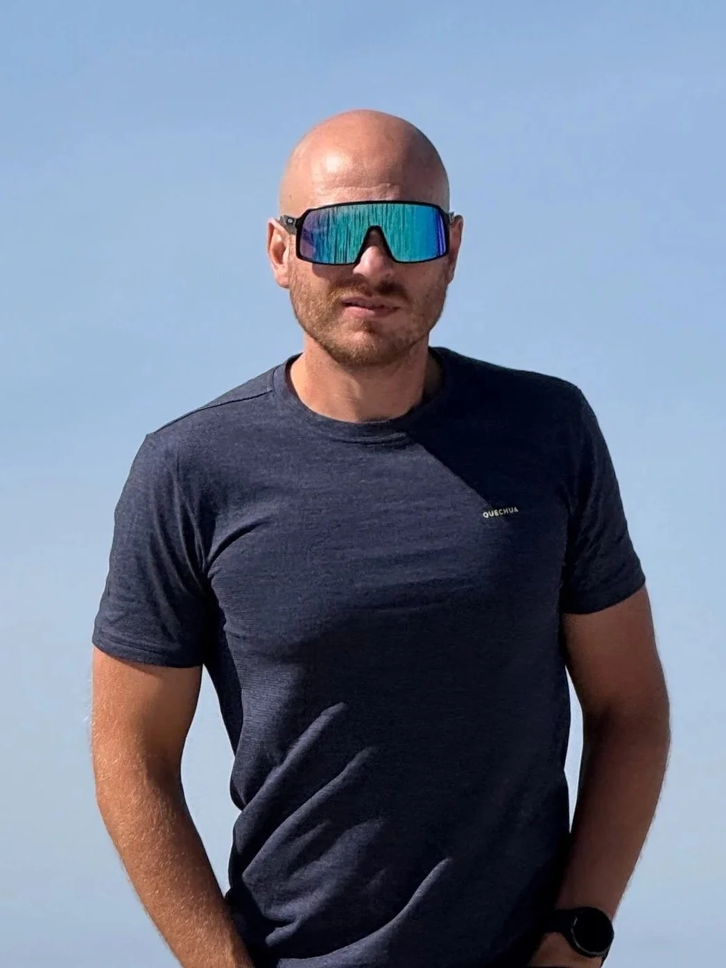 Mann mit Brille und dunklem T-Shirt vor blauem Himmel.