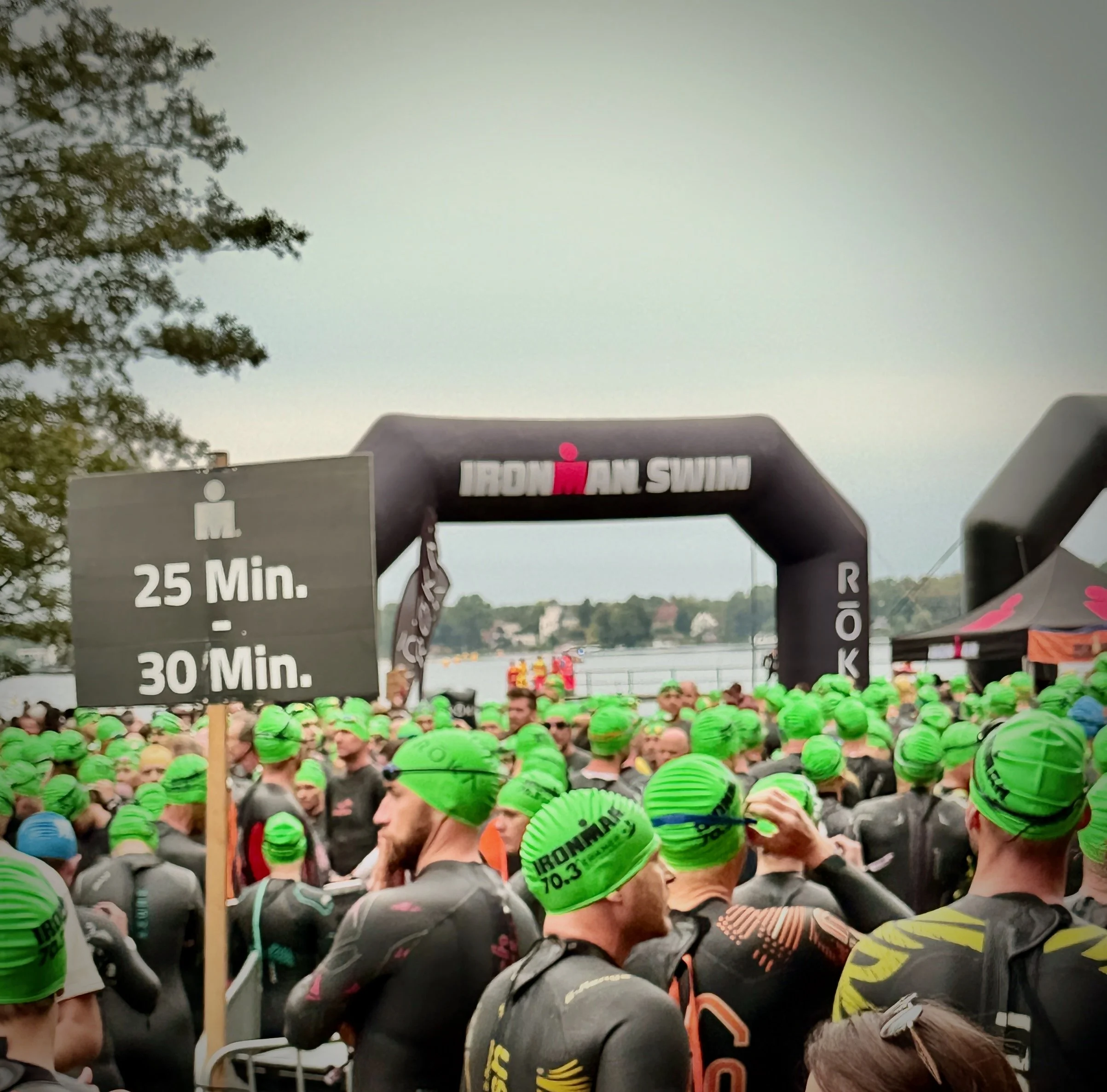 Viele Teilnehmer in grünen Helmen vor einem Startbogen für einen Ironman-Wettbewerb. Es scheint der Beginn eines Rennens zu sein.