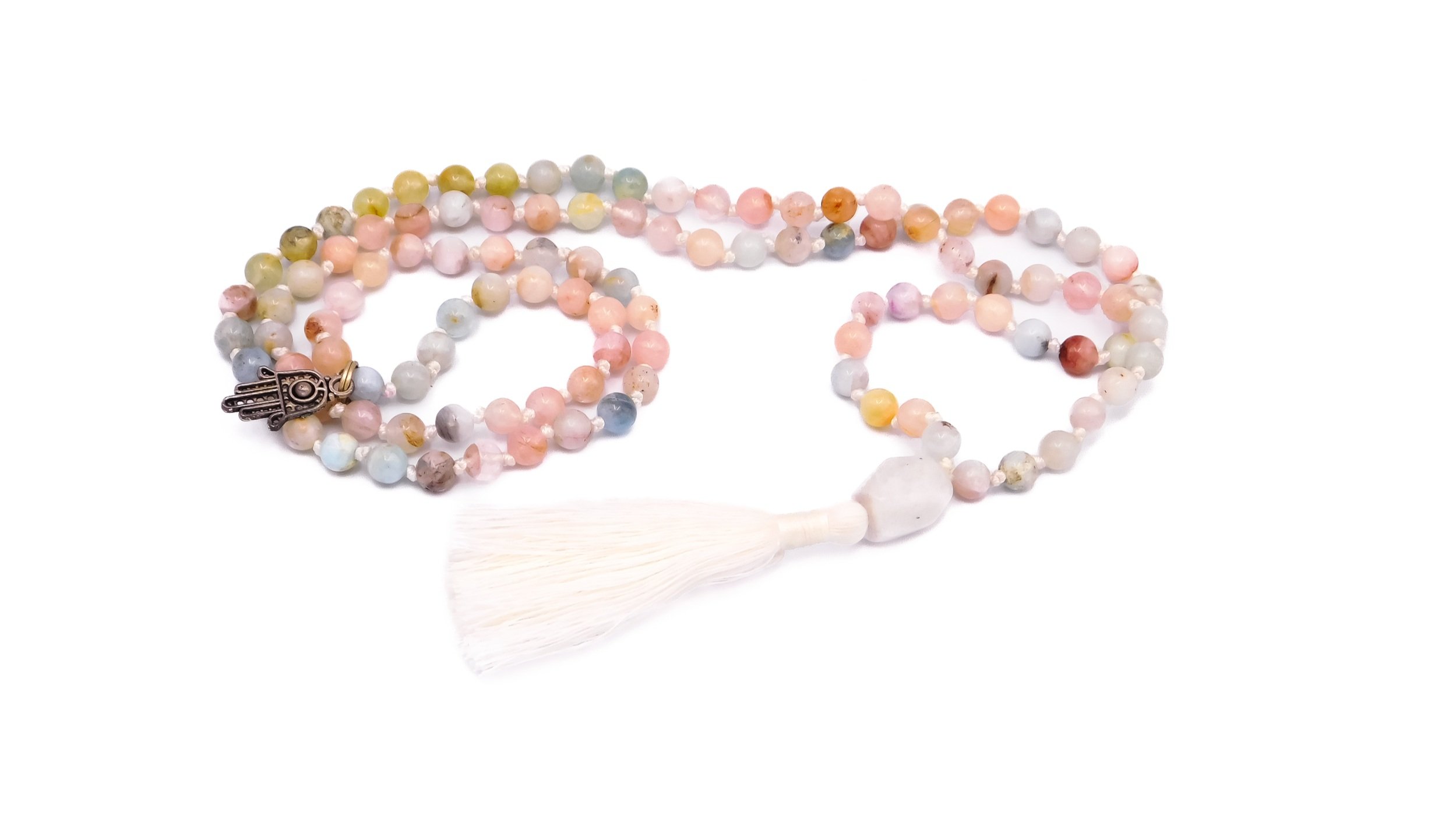 A beaded necklace with multicolored round stones, a white tassel, and a Hamsa hand charm, placed on a white surface.