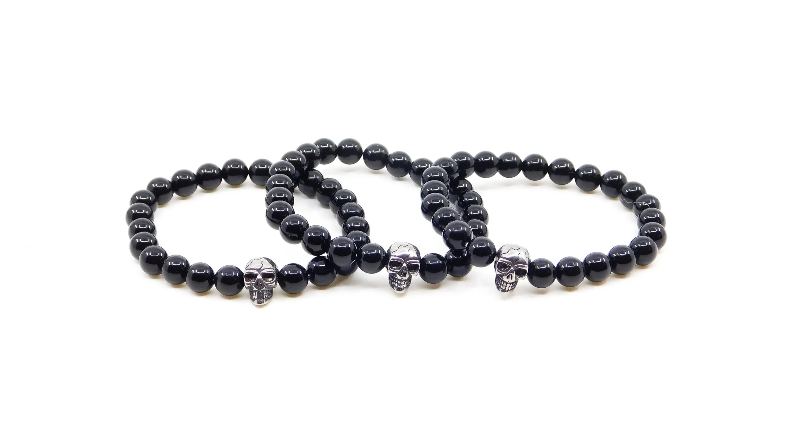 Set of three black beaded bracelets with silver skull charms on a white background.